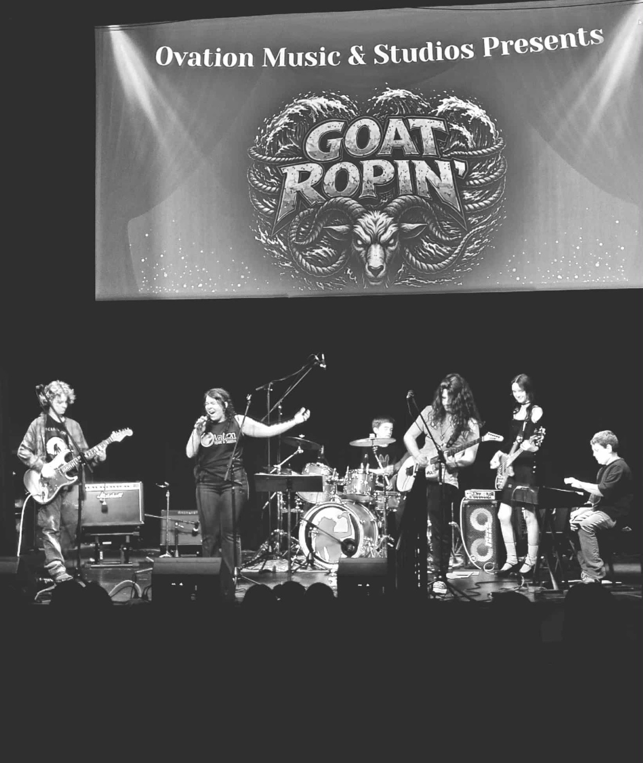 Ovation RockShop band performing on stage under a "Goat Ropin'" show screen.