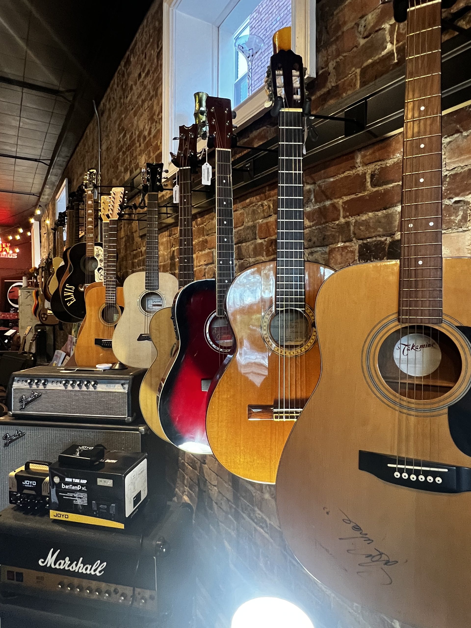 Guitars and amplifiers on display along a brick wall at Ovation Music & Studios.