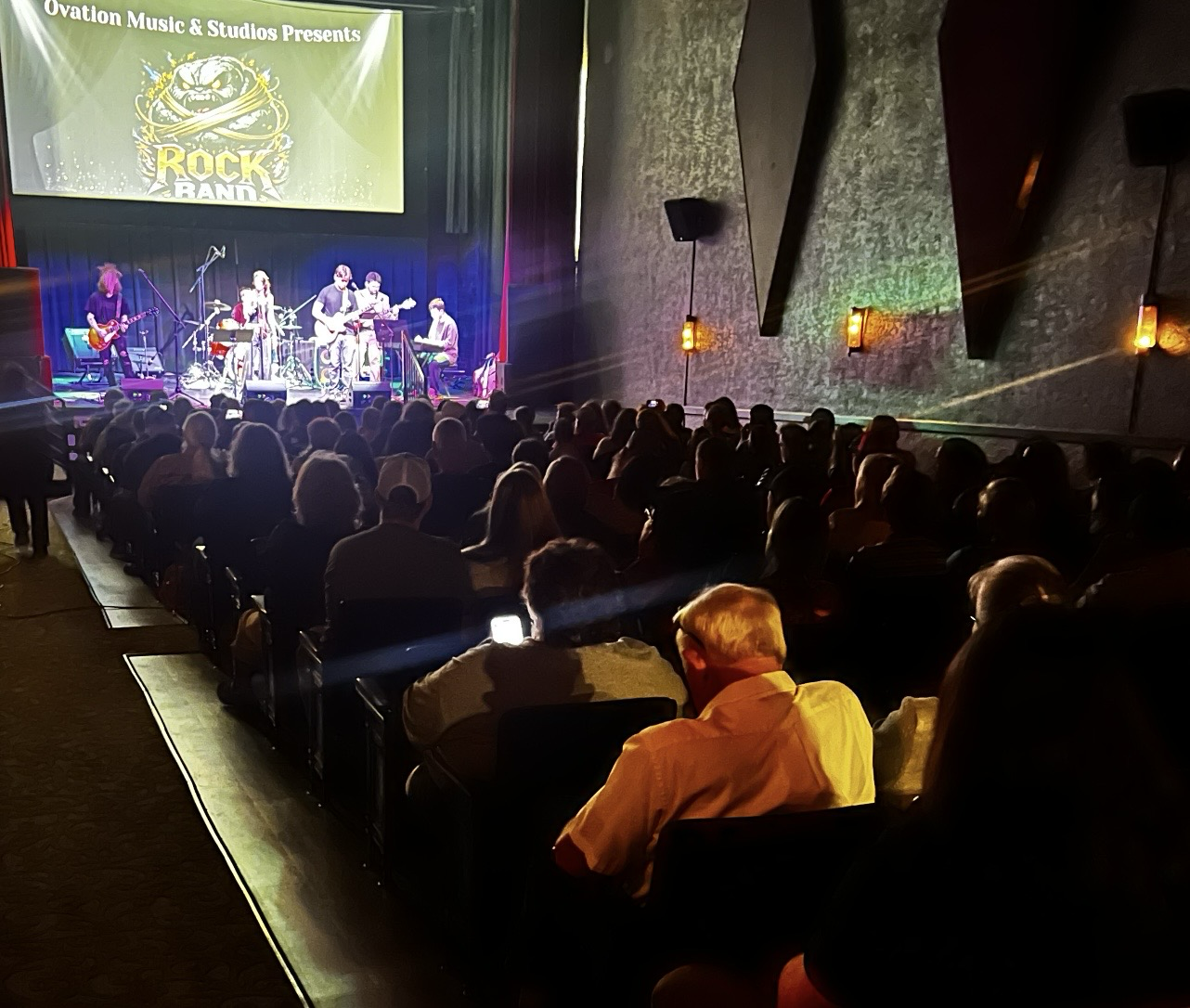 Audience watching an Ovation RockShop band perform on stage.